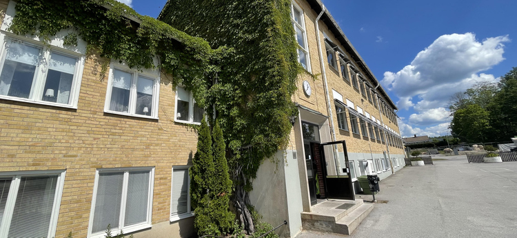 Tegelbyggnad med grön klätterväxt på fasaden. Björsäter skola.
