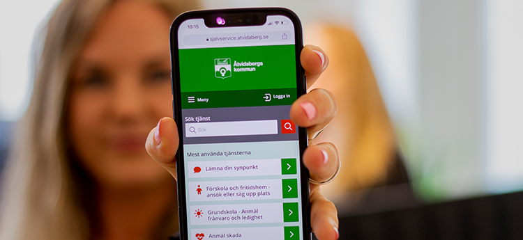 Kvinna som håller fram en mobiltelefon med Åtvidabergs kommuns självserviceportal.