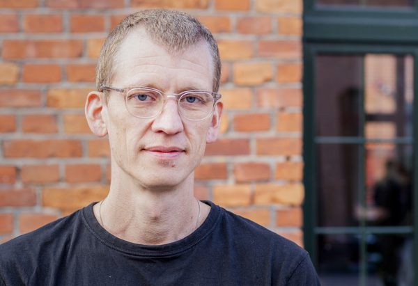 Sven står framför en tegelvägg.
