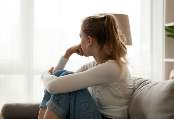 Flicka som sitter i en soffa och tittar ut genom fönstret.